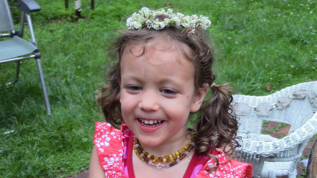 This is my daughter "smiling" with a hairstyle chosen by her (surprise) when she spontaneously went hunting for two hairbands to put her hair in two ponytails. (Her grandmother wave the flower wreath.)